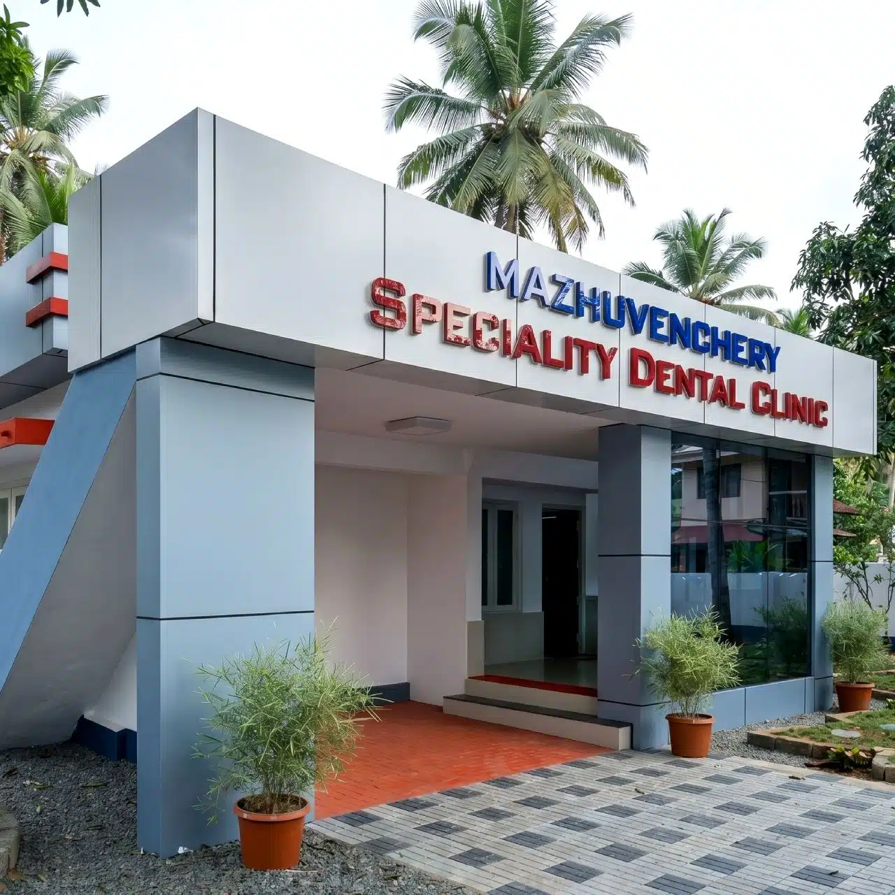 Exterior view of Mazhuvenchery Speciality, a modern dental clinic in Athani, featuring a clean building, clear signage, and potted tropical plants.